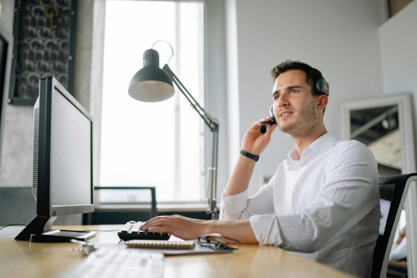 Male customer service agent taking a call in front of a computer, demonstrating the qualities of great customer service.