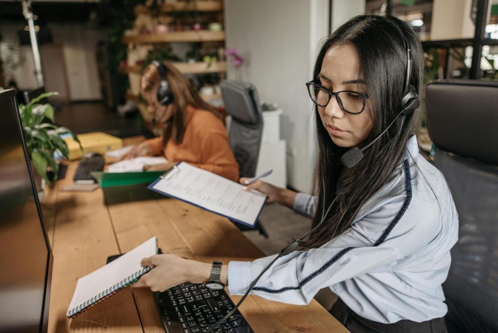 Call center agent providing saas customer service support in front of desktop while notes in hand